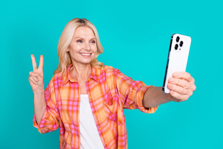 Photo of pleasant person blond hair dressed checkered shirt make selfie on smartphone showing v-sign...