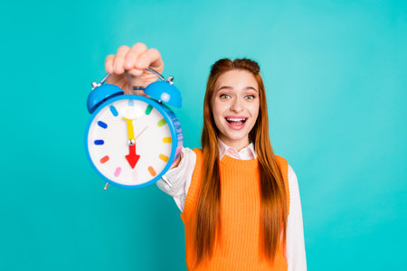 Photo of cheerful funny cute woman wear stylish orange clothes arm hold retro classic bell ring clock isolated on cyan color backgroundの写真素材