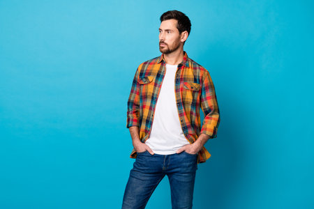 Photo of handsome cool man dressed plaid shirt hands in pockets look at business offer empty space isolated on blue color backgroundの写真素材
