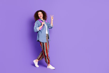Full body portrait of pretty young woman show v-sign walk empty space wear denim shirt isolated on...
