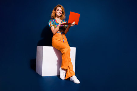 Full body portrait of nice young lady use laptop empty space wear top isolated on dark blue color backgroundの写真素材