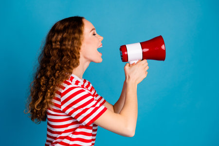 Side profile photo of adorable woman with wavy hairdo dressed striped t-shirt shout in loudspeaker isolated on blue color backgroundの写真素材