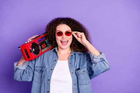 Portrait of pretty young woman hold boombox empty space wear denim shirt isolated on purple color backgroundの写真素材