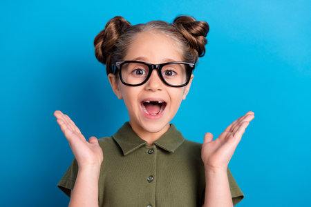 Portrait of cute sweet schoolkid impressed kindergarten gift news wear khaki t shirt isolated blue shine color backgroundの写真素材