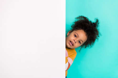 Photo of curious funny small lady peek white placard empty space wear striped sweater isolated teal color backgroundの写真素材