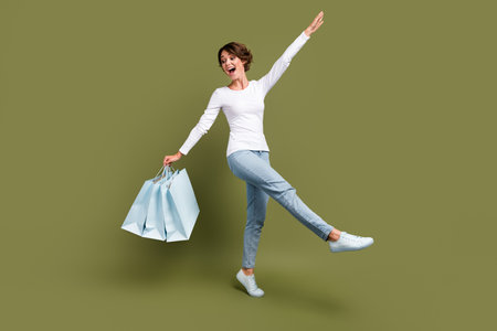 Full body photo of pretty young girl have fun happy walking shopping bags wear trendy white outfit isolated on khaki color backgroundの写真素材