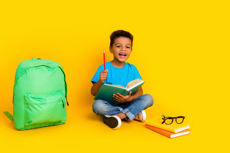 Full length photo of charming excited preteen boy wear blue t-shirt preparing homework isolated yellow color backgroundの写真素材