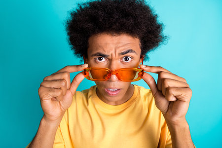 Photo of suspicious astonished man with afro hairdo wear oversize t-shirt staring at you hold...