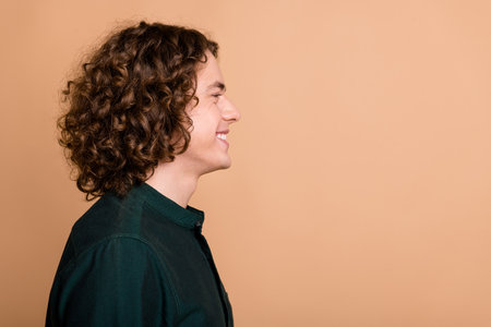 Profile side photo of positive handsome nice young man wear green trendy clothes look empty space isolated on beige color backgroundの写真素材
