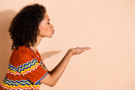 Side profile photo of lovely woman with perming coiffure wear knit t-shirt send air kiss to empty space isolated on beige color backgroundの写真素材