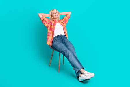Portrait of lovely cute senior woman wear checkered trendy clothes sit chair isolated on cyan color backgroundの写真素材