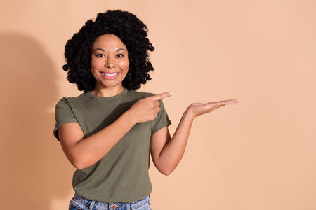 Photo portrait of pretty young woman hand hold point empty space dressed trendy khaki outfit isolated on beige color backgroundの写真素材