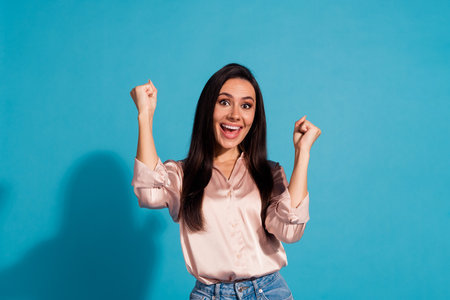 Portrait of overjoyed girl with long hairstyle wear silk blouse clenching fists scream yeah win bet isolated on blue color backgroundの写真素材