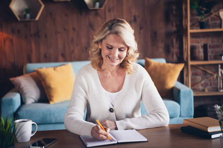 Portrait of aged lady hold pen write notes notepad wear white cardigan loft interior house indoorsの写真素材