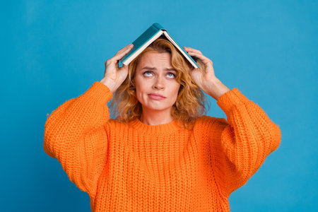 Photo of sad upset adorable woman wear stylish orange clothes hold book look empty space isolated on blue color backgroundの写真素材