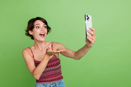 Photo of lovely cute girl wear stylish clothes hold modern device video live stream talk blank space isolated on green color backgroundの写真素材