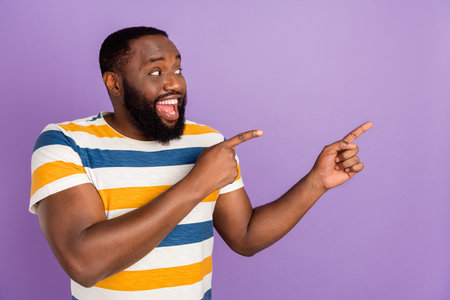 Photo of positive funky man wear striped t-shirt looking showing two fingers empty space isolated violet color backgroundの写真素材