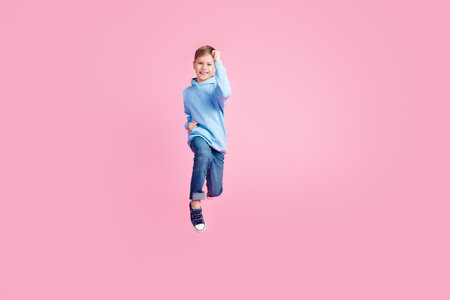 Full size photo of delighted crazy schoolchild jump raise fists achieve empty space isolated on pink color backgroundの写真素材
