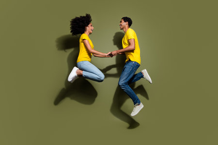 Full size photo of two young people rejoice hold arms jump wear t-shirt isolated on khaki color backgroundの写真素材