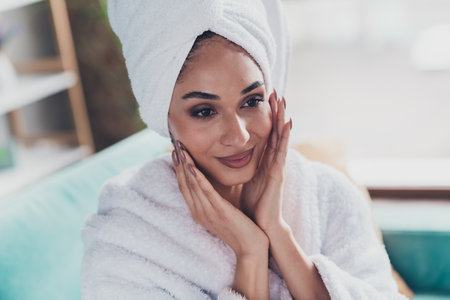 Photo of pretty lovely lady sit sofa fingers touch face apply hydration lotion wear bathrobe turban hotel indoorsの写真素材