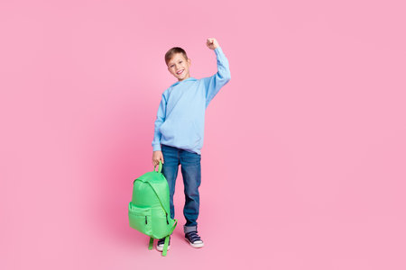 Full size photo of delighted cheerful schoolkid hold backpack raise fist empty space isolated on pink color backgroundの写真素材