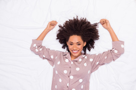 Photo of cute cheerful lady wear pajama lying bed holding hair curls isolated white color backgroundの写真素材
