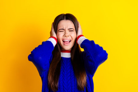Photo portrait of pretty teen girl cover ears avoid noise crying wear trendy knitwear blue outfit isolated on yellow color backgroundの写真素材