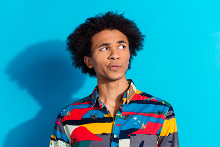 Photo portrait of handsome young guy look skeptical empty space dressed stylish print garment isolated on blue color backgroundの写真素材