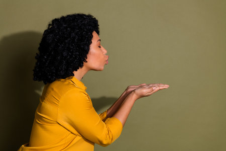 Portrait of pretty lady hands send air kiss empty space wear yellow shirt isolated on khaki color backgroundの写真素材