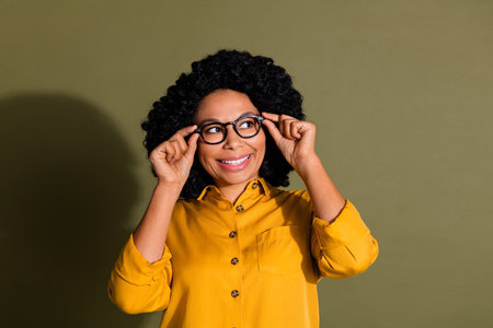 Portrait of pretty lady touch glasses look empty space wear yellow shirt isolated on khaki color backgroundの写真素材