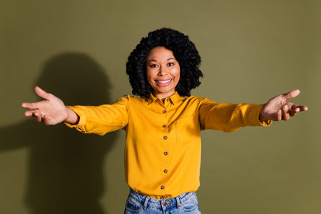 Portrait of nice young woman arms welcome you wear yellow shirt isolated on khaki color backgroundの写真素材