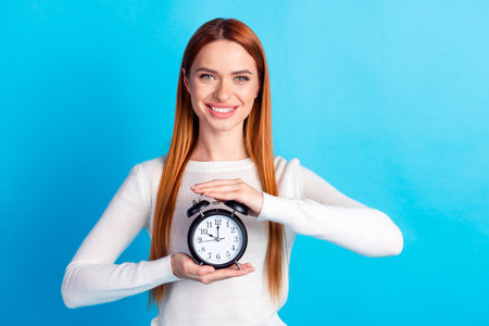 Photo portrait of attractive young woman hold alarm clock dressed stylish white clothes isolated on...