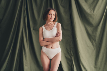 Unretouched photo of attractive old woman cross arms wear underclothes isolated green color linen backgroundの写真素材