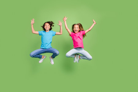 Full length photo of positive cheerful friends wear t-shirts jumping high rising hands arms isolated green color backgroundの写真素材