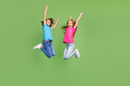 Full length photo of sweet lucky friends wear t-shirts jumping high rising fists empty space isolated green color backgroundの写真素材