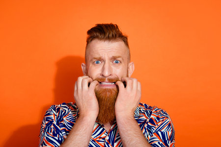 Photo of nervous scared guy dressed print shirt biting fingers emtpy space isolated orange color backgroundの写真素材