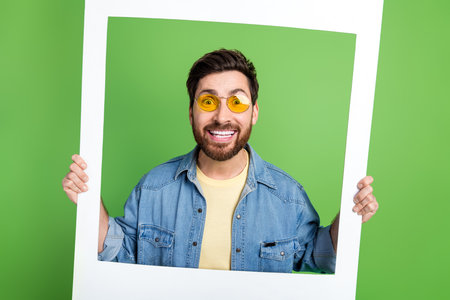 Photo of cheerful impressed guy wear denim jacket tacking photo isolated green color backgroundの写真素材