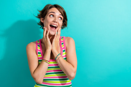 Portrait of cheerful nice impressed lady hands touch cheeks open mouth look empty space isolated on turquoise color backgroundの写真素材