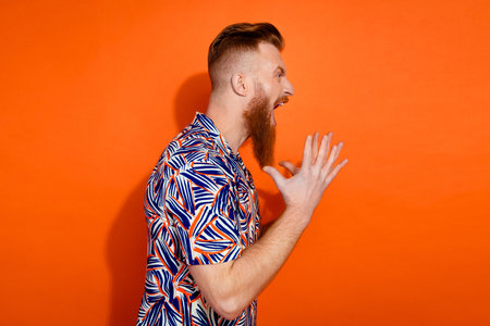 Photo of furious angry guy dressed print shirt screaming empty space isolated orange color backgroundの写真素材