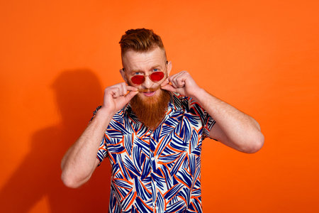 Photo of brutal stylish guy with red beard in sunglass touching mustache advertising barershop...
