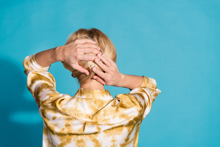 Photo portrait of attractive mature woman arrange hold hair back view dressed stylish formalwear clothes isolated on cyan color backgroundの写真素材