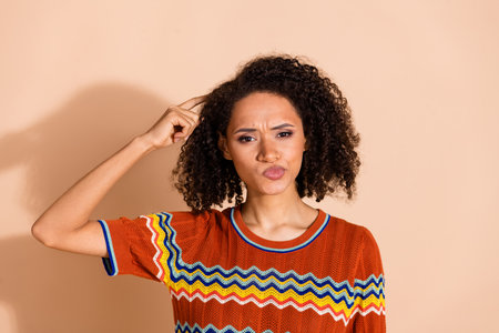 Portrait of pensive confused girl with wavy hairdo dressed ornament t-shirt finger scretching head isolated on pastel color backgroundの写真素材