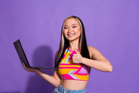 Photo of attractive lovely cute girl wear stylish clothes hand hold recommend device thumb up isolated on purple color backgroundの写真素材