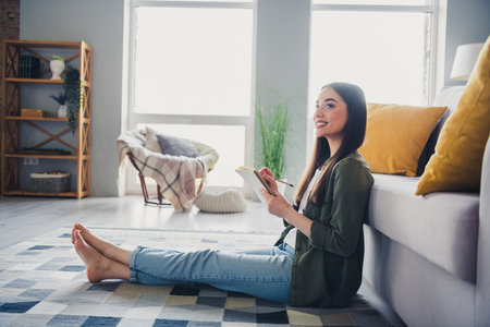 Full size photo of pretty young lady sit floor hold notepad think wear green shirt weekend modern apartment indoorsの写真素材