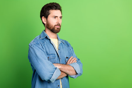 Photo of handsome serious guy wear denim jacket arms folded looking empty space isolated green color backgroundの写真素材