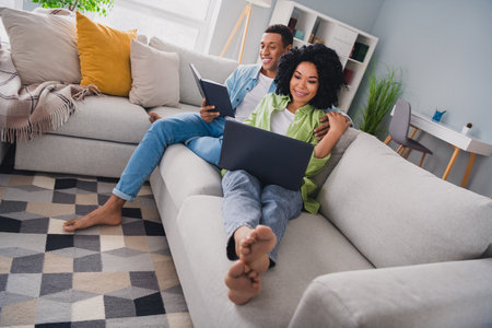 Full size photo of nice young man girl sit sofa work remotely netbook read book modern interior indoors cozy daylight apartment living roomの写真素材
