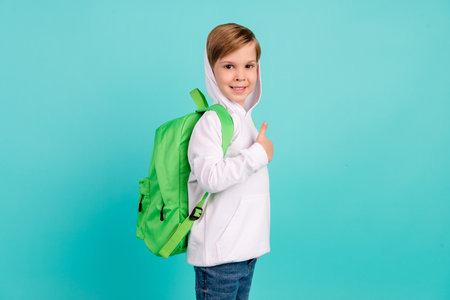 Photo of cute boy ready back to school buy new schoolbag make thumb fine symbol isolated teal color backgroundの写真素材
