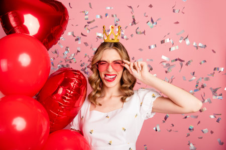 Photo portrait of lovely young woman balloons crown confetti flirty dressed stylish white garment hairdo isolated on pink color backgroundの写真素材