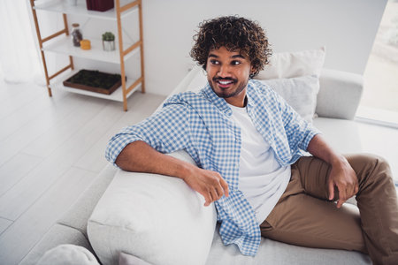 Photo of cool good mood man wear checkered shirt staying home relaxing couch indoors house apartment roomの写真素材