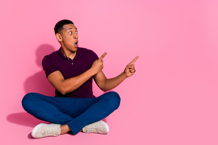 Full size photo of attractive young man sit point scared empty space dressed stylish violet clothes isolated on pink color backgroundの写真素材